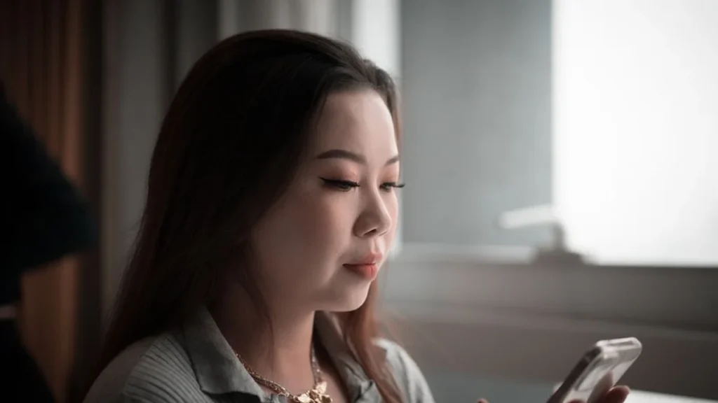 A woman in profile looking thoughtfully near a smartphone on a wooden surface.
