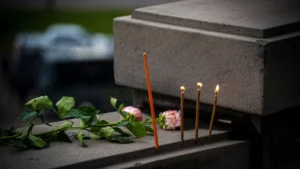 A white rose and a lit candle on a dark reflective surface for memorial.