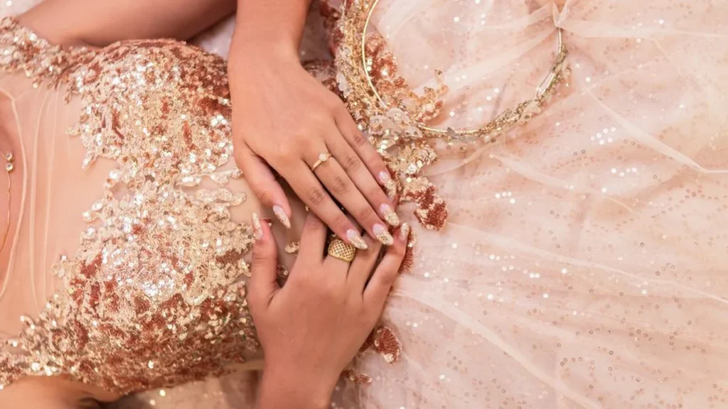 Shimmering pink sequined fabric with diamond jewelry and red nail polish on a reflective surface.