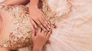 Shimmering pink sequined fabric with diamond jewelry and red nail polish on a reflective surface.