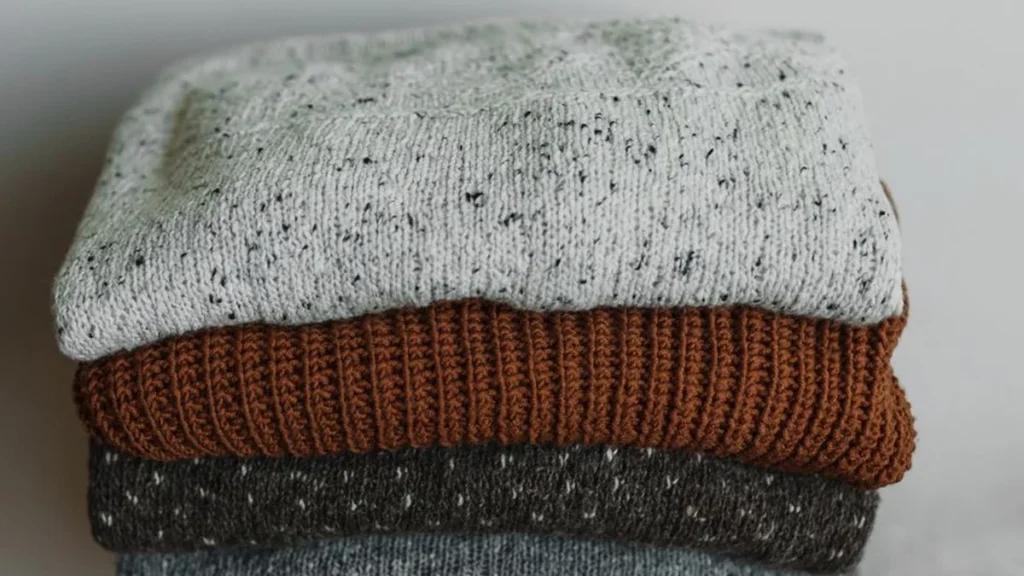 A brown mohair sweater and dark indigo denim jeans resting on a reflective chrome surface.