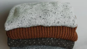 A brown mohair sweater and dark indigo denim jeans resting on a reflective chrome surface.
