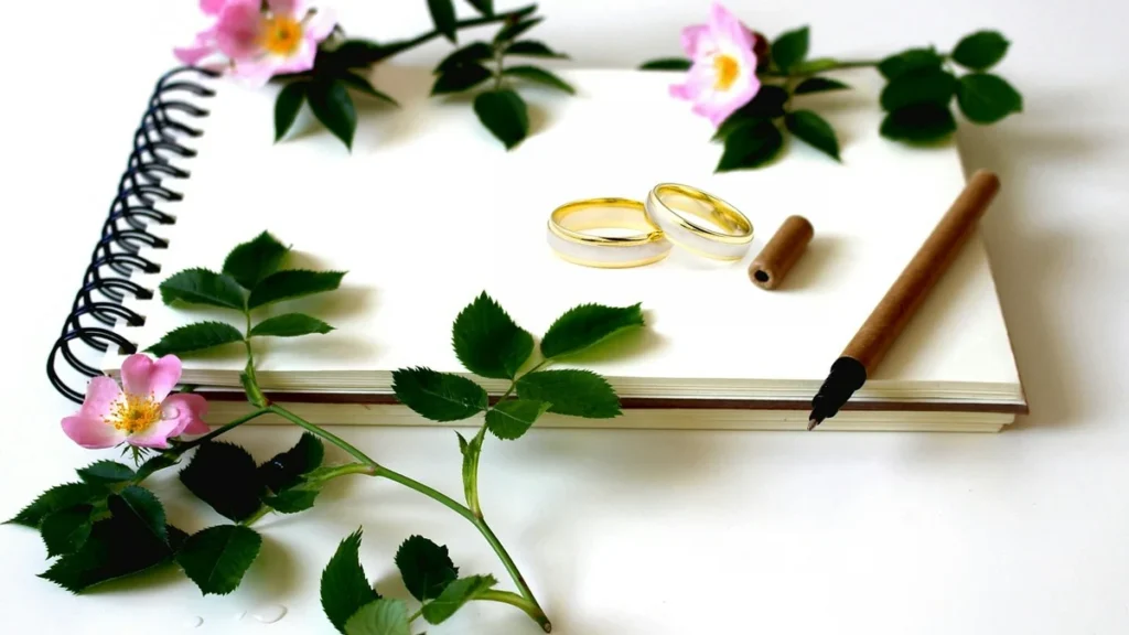 A wedding ring next to a fountain pen and children's books on a dark surface.