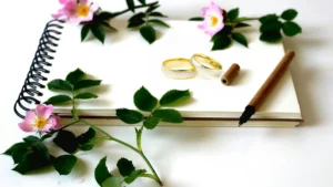 A wedding ring next to a fountain pen and children's books on a dark surface.