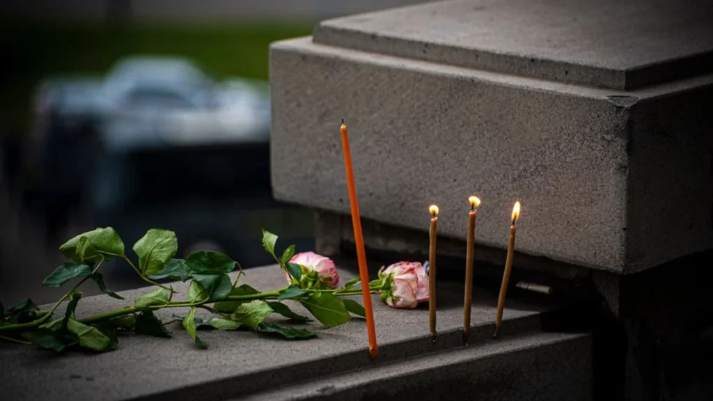 A white rose and lit candle next to a framed photo on a reflective surface.