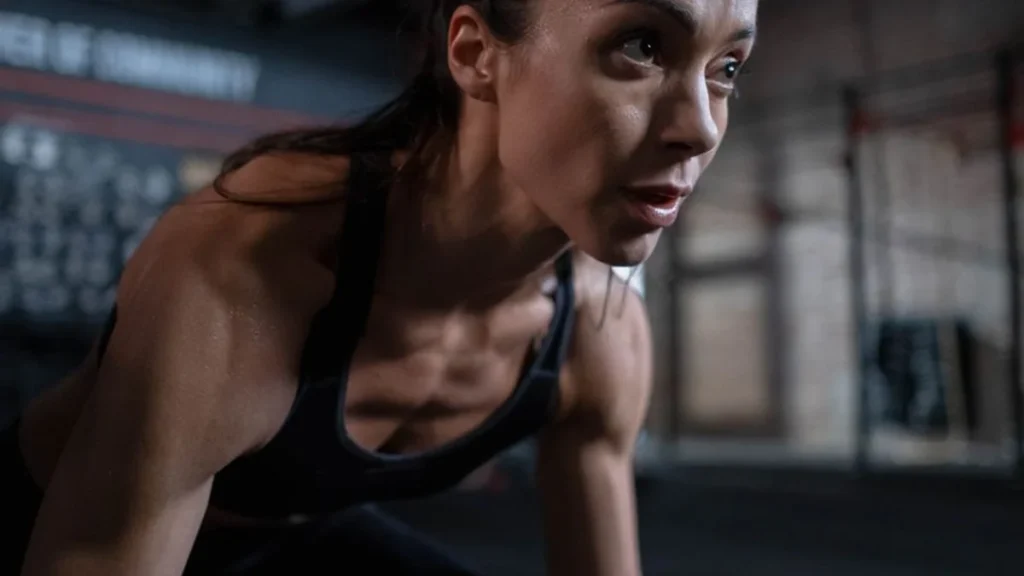 A close-up portrait of a focused woman sweating after an intense high-intensity interval training workout.