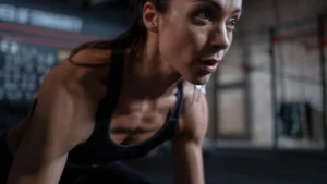 A close-up portrait of a focused woman sweating after an intense high-intensity interval training workout.