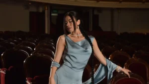 A cornflower blue silk couture gown with a single floral detail on a white pedestal.
