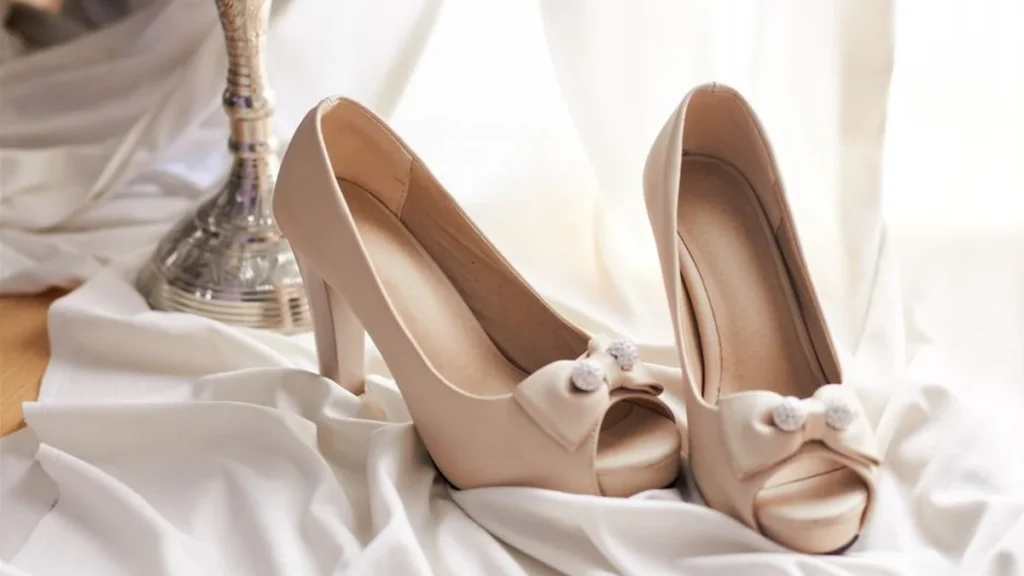 High-heeled shoes and silk fabric resting on a reflective chrome surface.